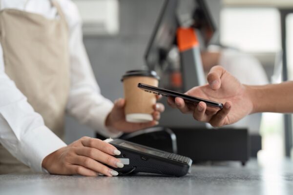 カフェのカウンターでスマートフォンを提示してコーヒーを購入する利用客の手元